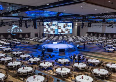CSUSA main session room with round tables and a giant center hung screen array